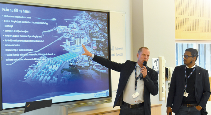 Två män i kostym som håller tal framför en skiss av framtidens containerterminal i Helsingborg